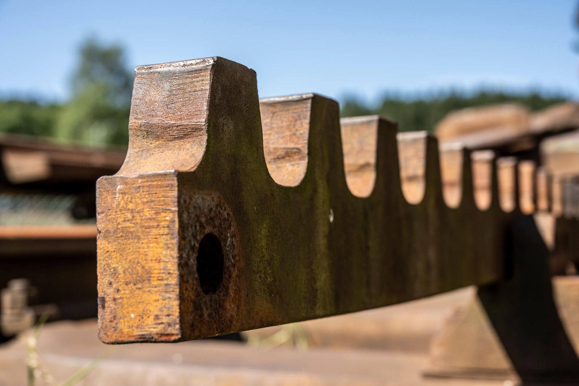 Rostige Metallkonstruktion mit Aussparungen, im Vordergrund scharf, Hintergrund unscharfe Landschaft und Himmel.